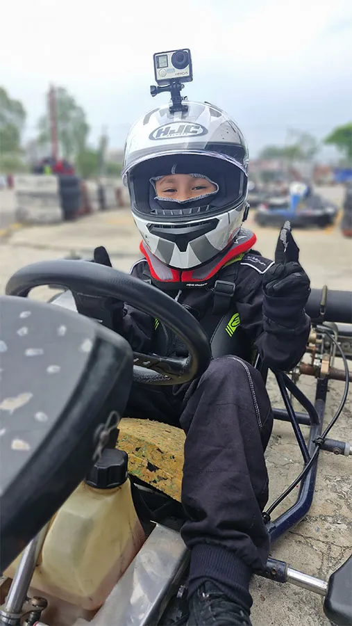 Enea sitting in his kart, wearing his helmet and smiling as he poses for the camera.
