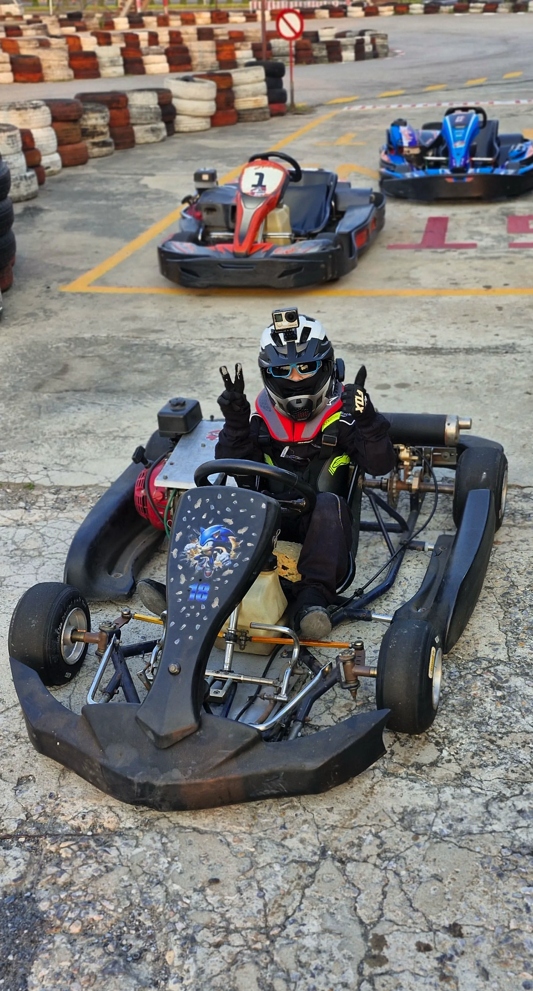 Enea sitting in his racing kart, smiling and holding up a victory sign with his fingers.